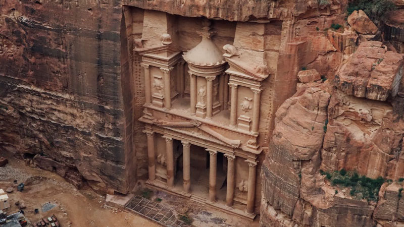 Scenic view of Petra in Jordan, featuring the iconic Treasury carved into rose-red sandstone cliffs, surrounded by rugged desert landscapes